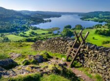 A morning shot of Lake Windermere and surrounding hills with a stone wall and stile in the foreground.