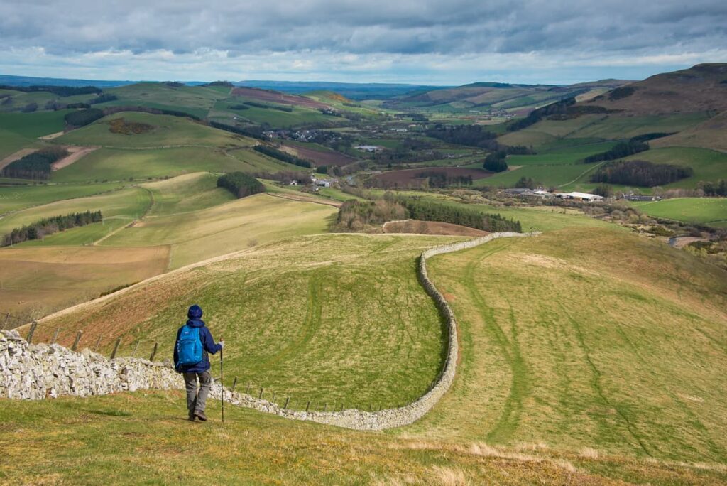 Walker with backpack enjoying spectacular panoramic views across the rolling Cheviot Hills landscape along St Cuthbert's Way trail