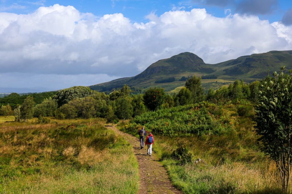 Hikers walking near Dumgoyne on the West Highland Way with lush green hills in the background – perfect for West Highland Way photos.