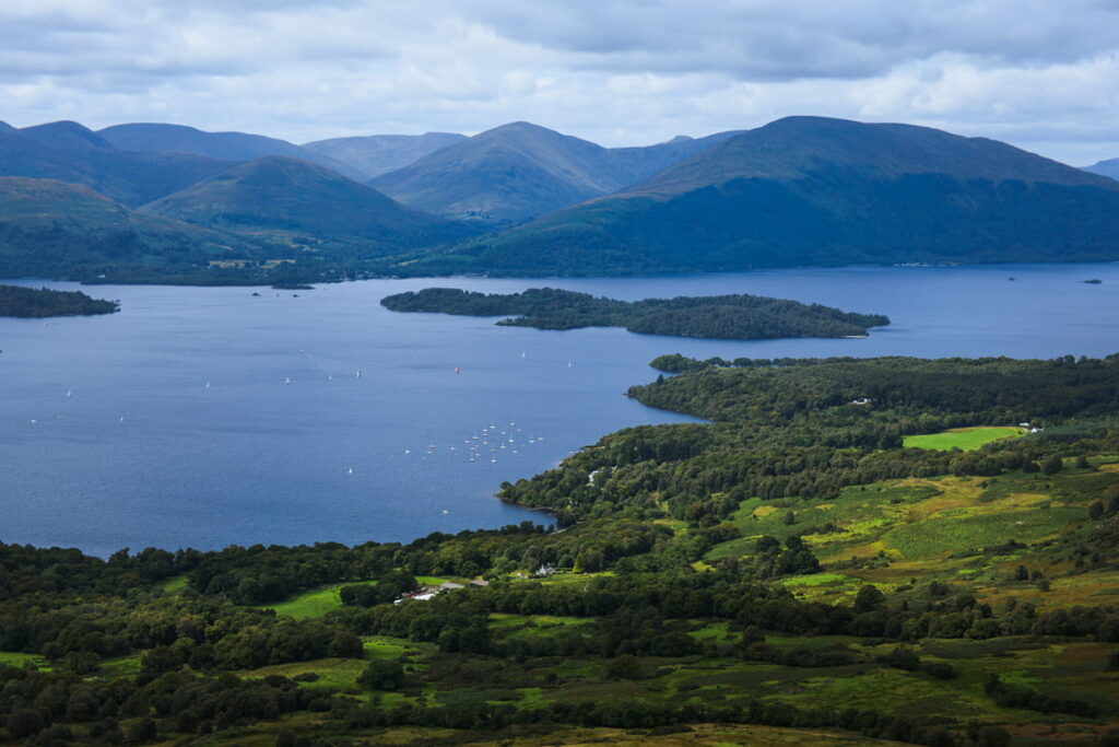 Sweeping vista from Conic Hill summit showing Loch Lomond's islands and wooded shores stretching toward distant Highland peaks