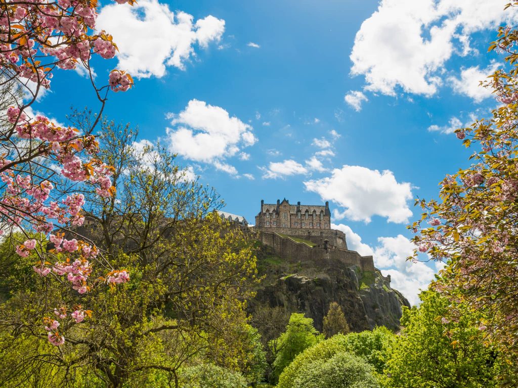 Edinburgh Castle in spring with fresh greenery, pink blossom, and blue skies, highlighting one of the best times to visit Scotland
