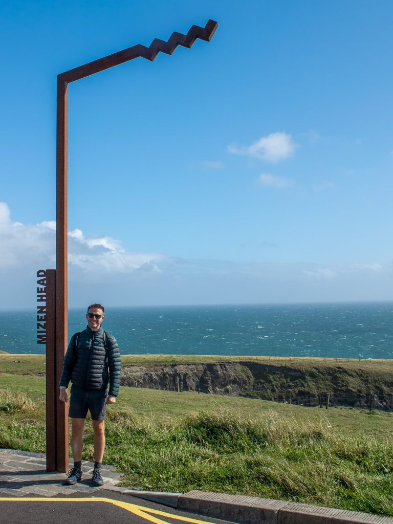 Scott from the Absolute Escapes team with one of Ireland's iconic Wild Atlantic Way signposts at Mizen Head.